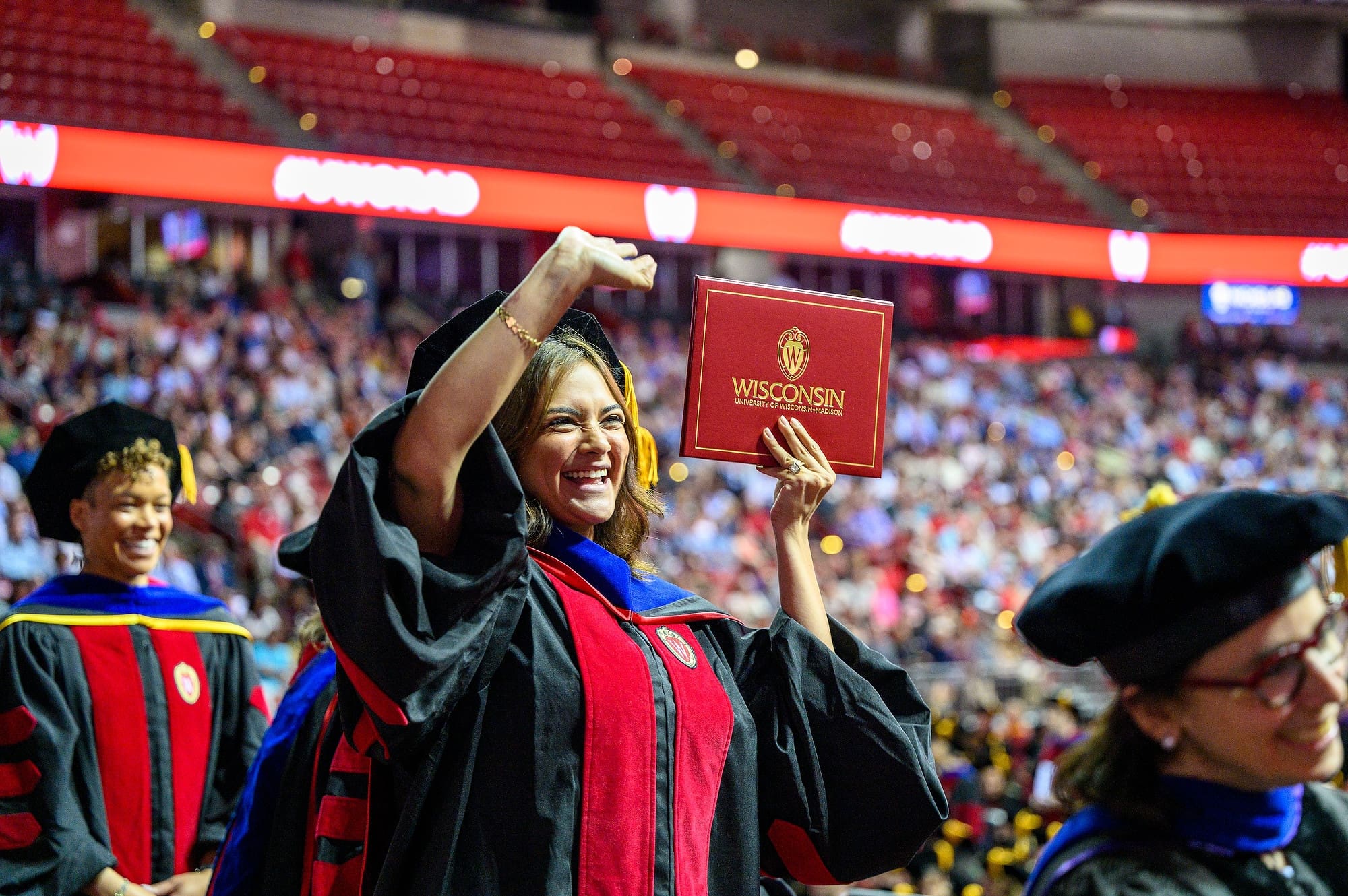A proud graduate waves to supporters in the audience as she displays her diploma.